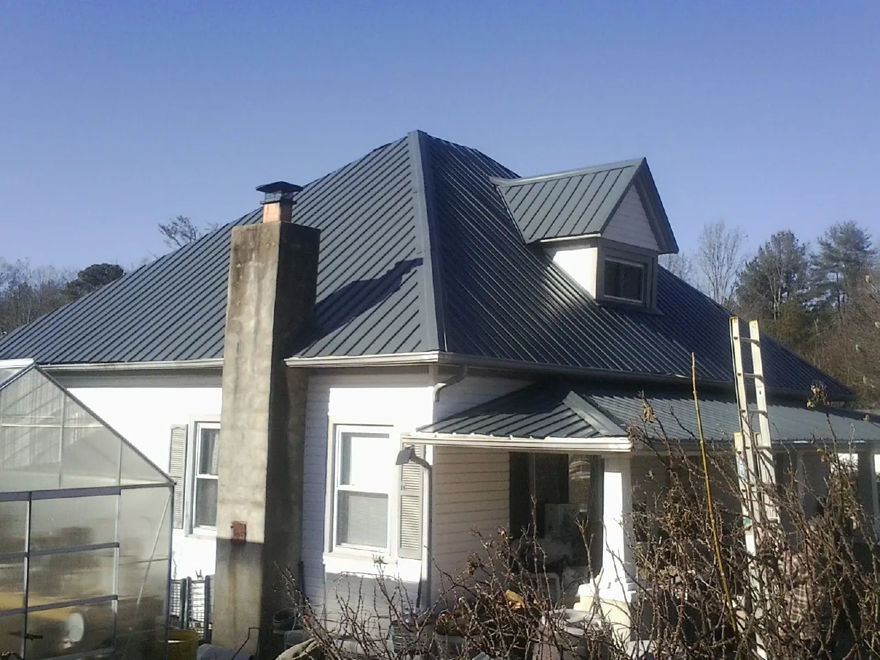 Dark blue standing seam metal roof on a white farmhouse with dormer — Slate & Tile Roof Repair by Roofing Brothers in Niota