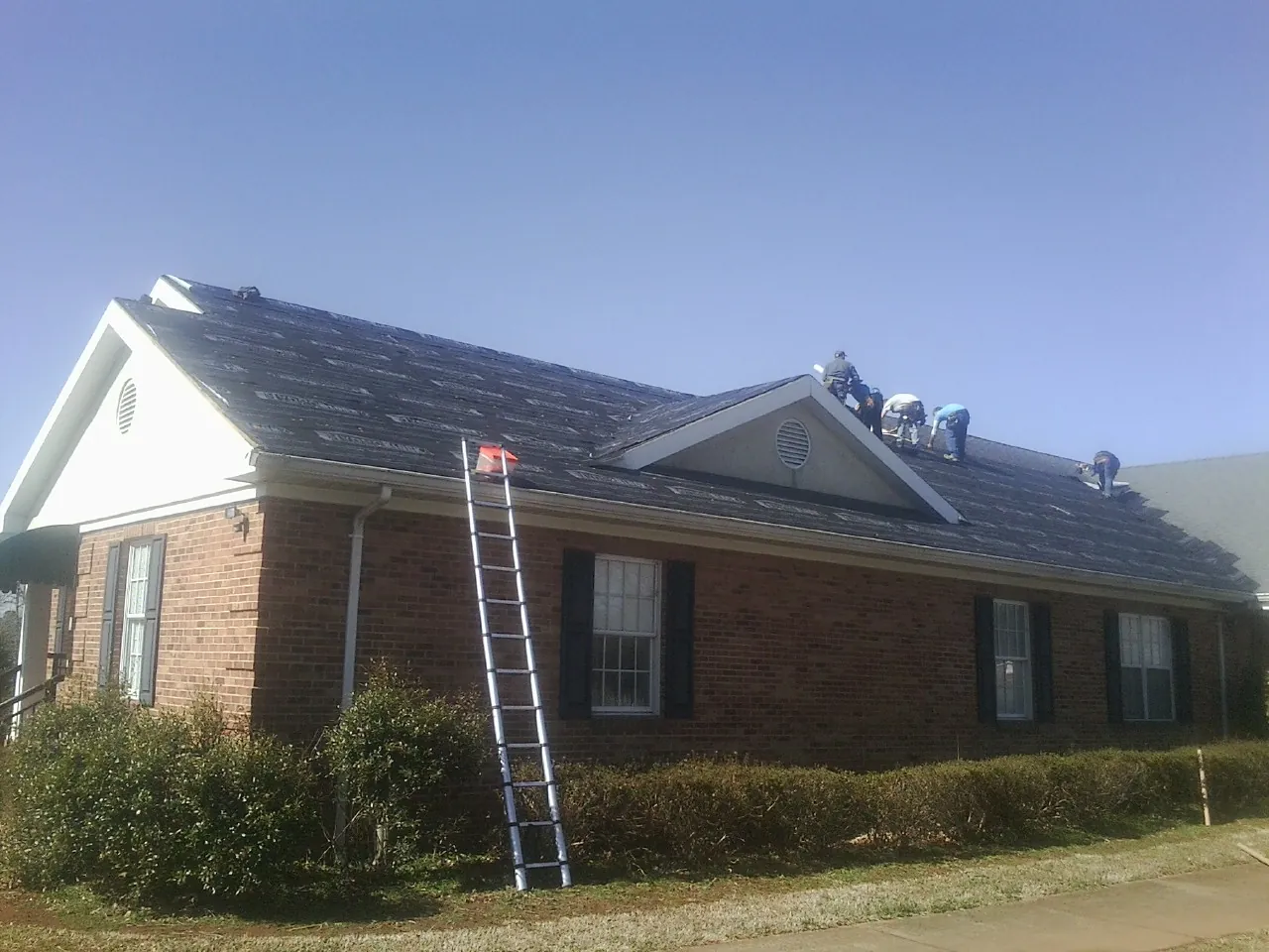 Crew tearing shingles off a brick ranch roof with a ladder set — Metal Roof Repair work by our crew in Niota