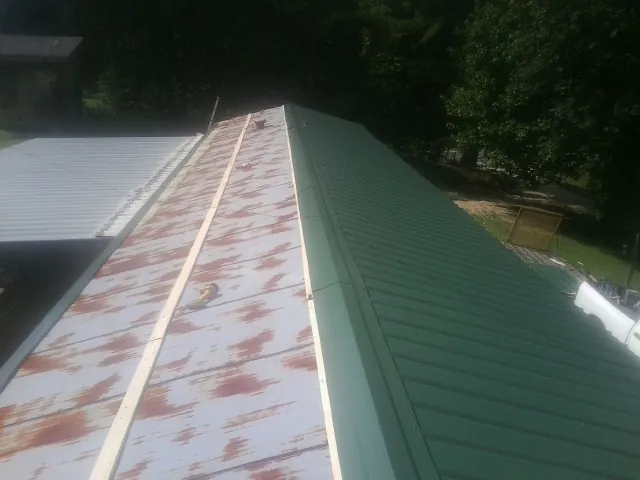 Old rusted panels beside newly installed green metal roofing — Wind Damage Roof Repair by Roofing Brothers in Niota