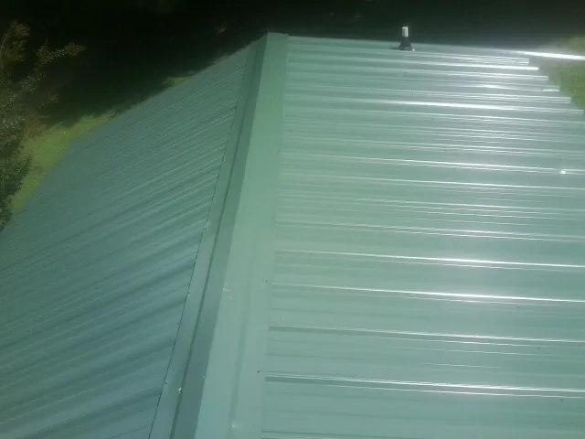 New green metal panels meeting at the ridge of a roof — Flat Roof Repair work by our crew in Niota