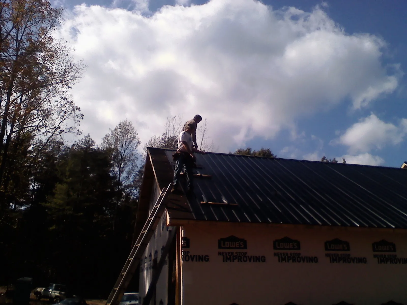Roofer fastening dark metal panels high against a cloudy sky, from a Roof Inspection job in Niota