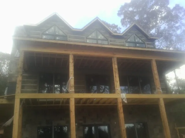 Dormers and porch framing on a large log home under construction — Roof Coating work by our crew in Niota
